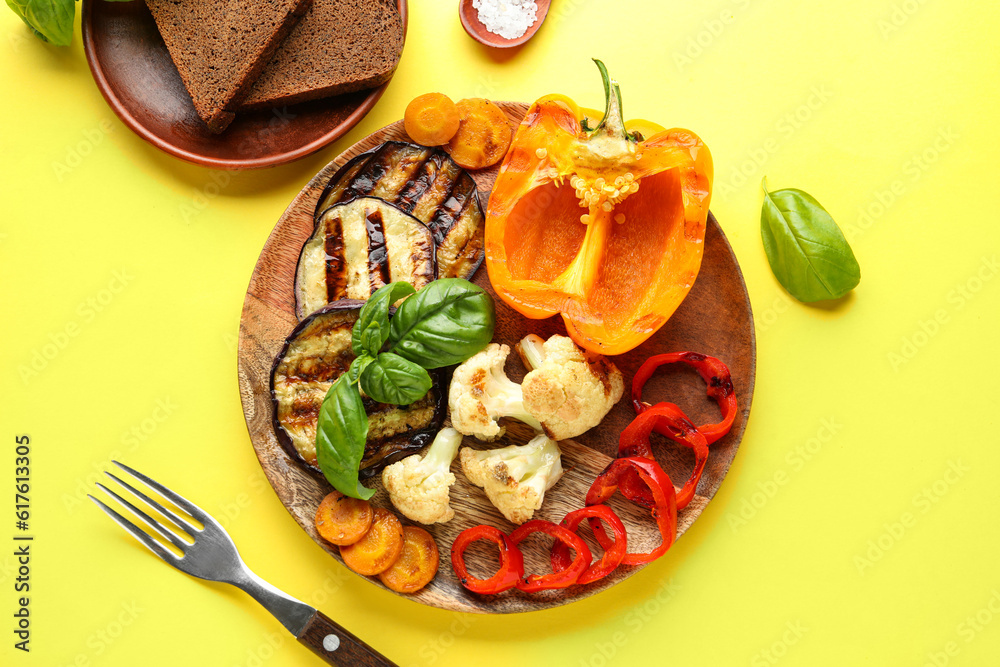 Plate with grilled vegetables and basil on yellow background