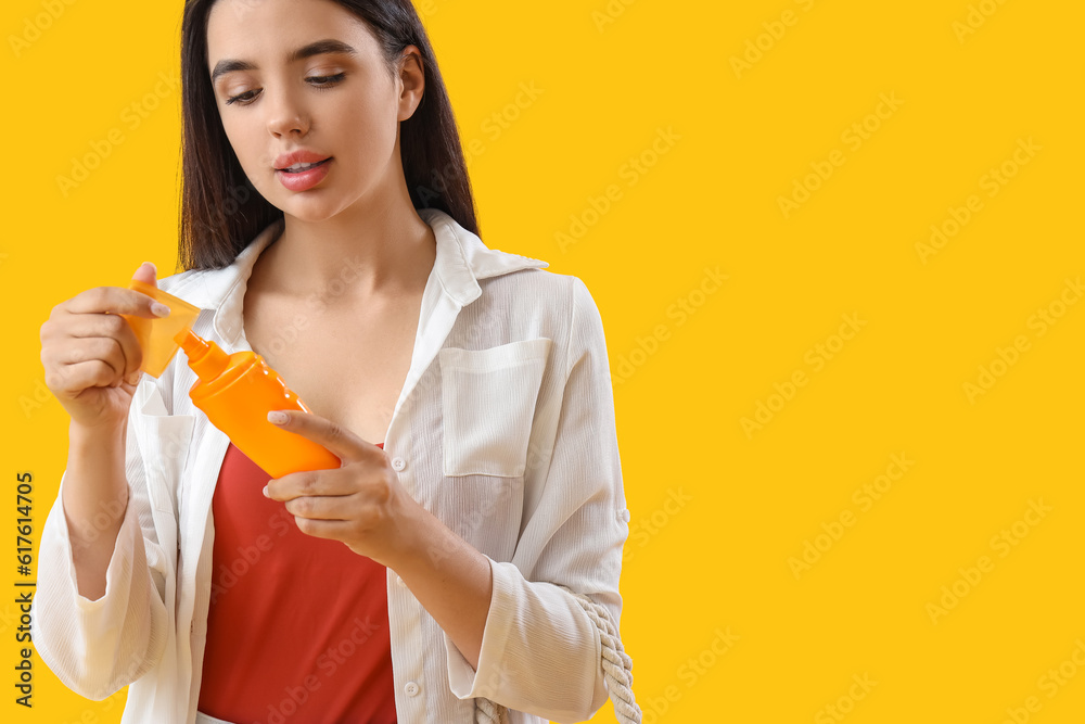 Young woman with sunscreen cream on yellow background