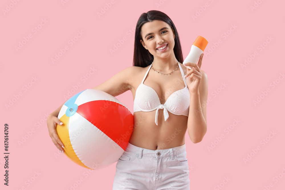 Young woman with sunscreen cream and beach ball on pink background