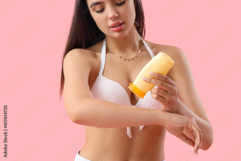 Young woman applying sunscreen cream on pink background, closeup