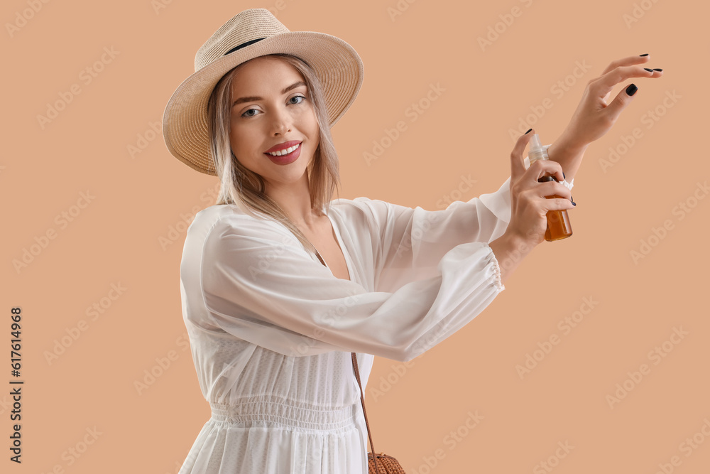 Young woman applying sunscreen cream on beige background