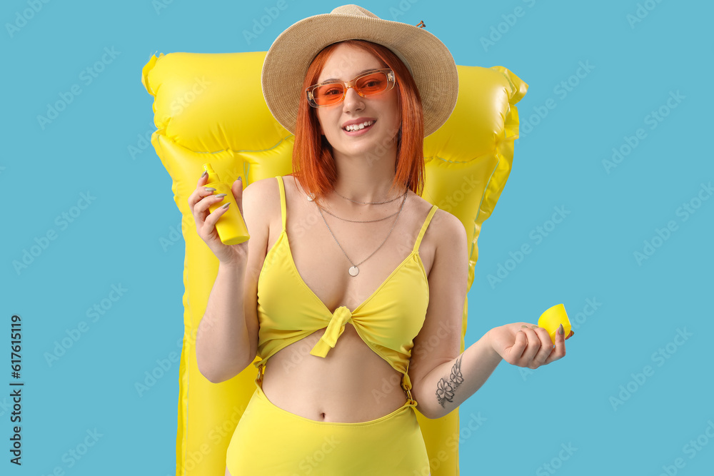 Young woman with sunscreen cream and inflatable mattress on blue background