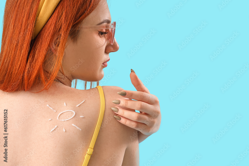 Young woman with sun made of sunscreen cream on blue background, back view