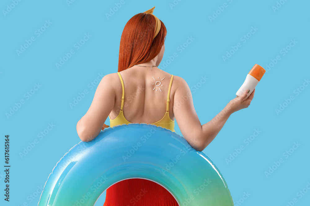 Young woman with sun made of sunscreen cream and inflatable ring on blue background, back view