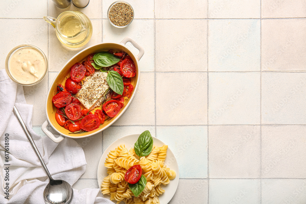 Baking dish with tasty tomatoes, feta cheese and pasta on white tile background