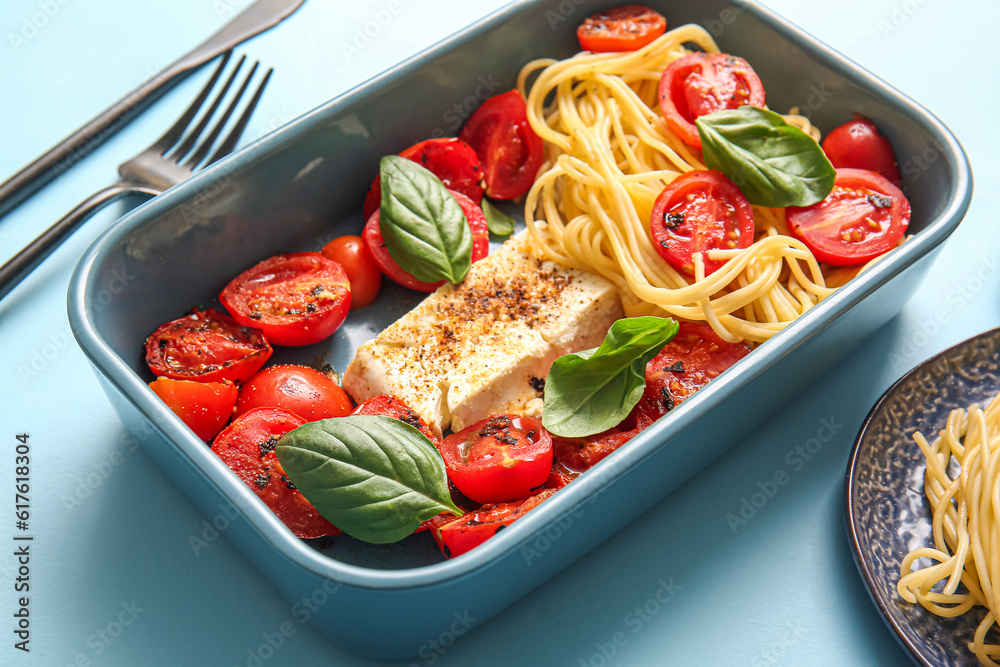 Baking dish of tasty pasta with tomatoes and feta cheese on blue background