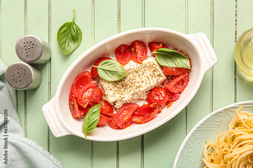 Baking dish with tasty tomatoes and feta cheese on green wooden background