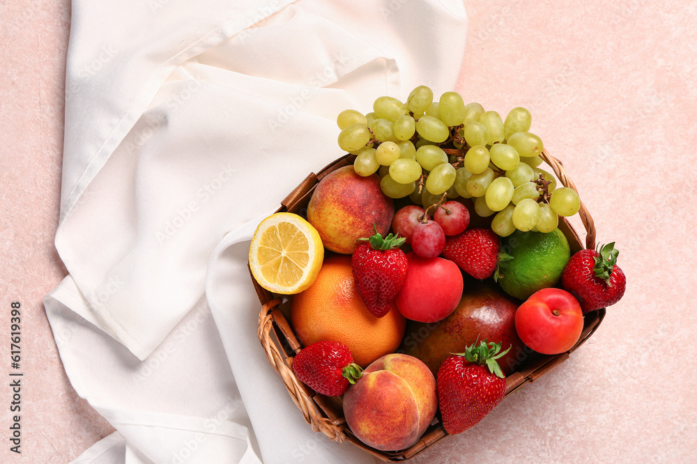 Wicker basket with different fresh fruits on pink background