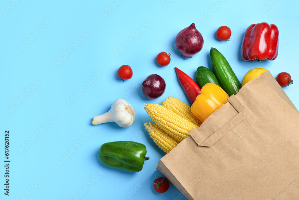 Paper bag with fresh vegetables on blue background