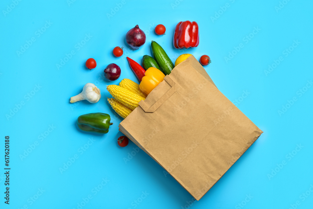 Paper bag with fresh vegetables on blue background