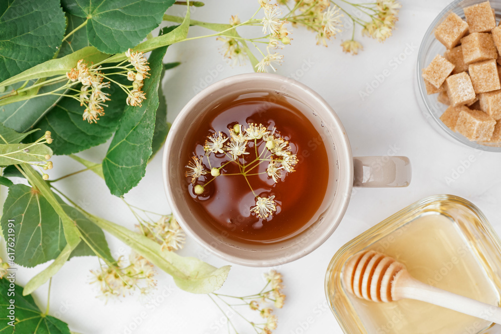 Cup of linden tea and bowl with honey on white table