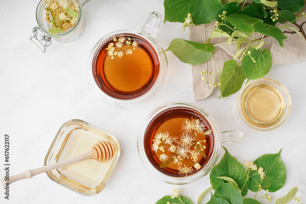 Glass cups of linden tea and bowls with honey on white background