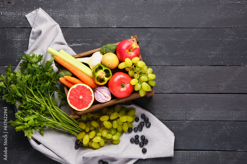 Box with different fresh fruits and vegetables on black wooden background