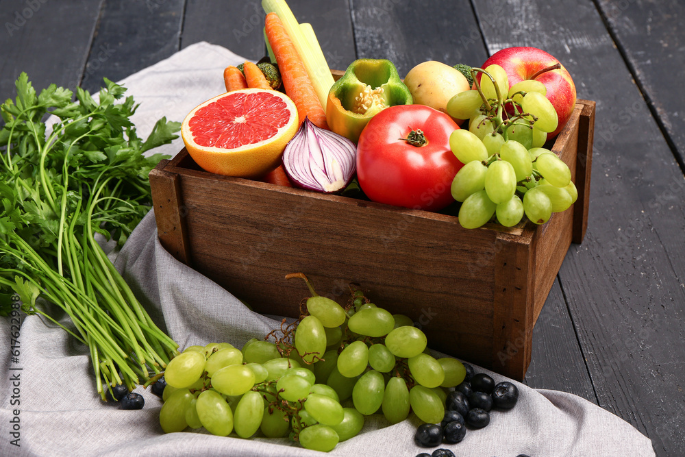 Box with different fresh fruits and vegetables on black wooden background