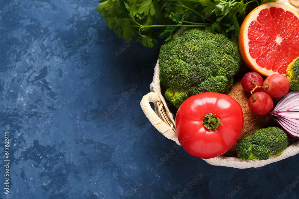 Wicker basket with different fresh fruits and vegetables on blue background, closeup