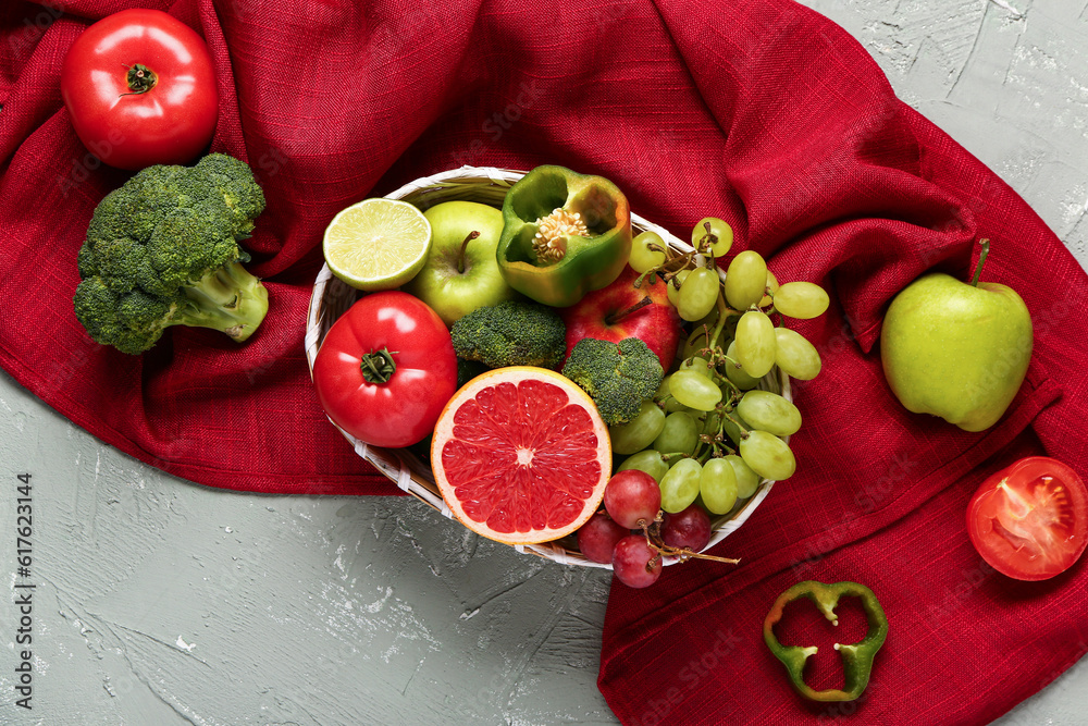 Wicker bowl with different fresh fruits and vegetables on grey background