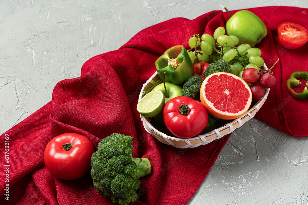 Wicker bowl with different fresh fruits and vegetables on grey background