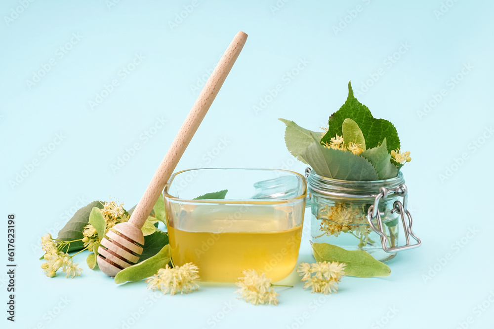 Glass bowl with linden honey and dipper on blue background