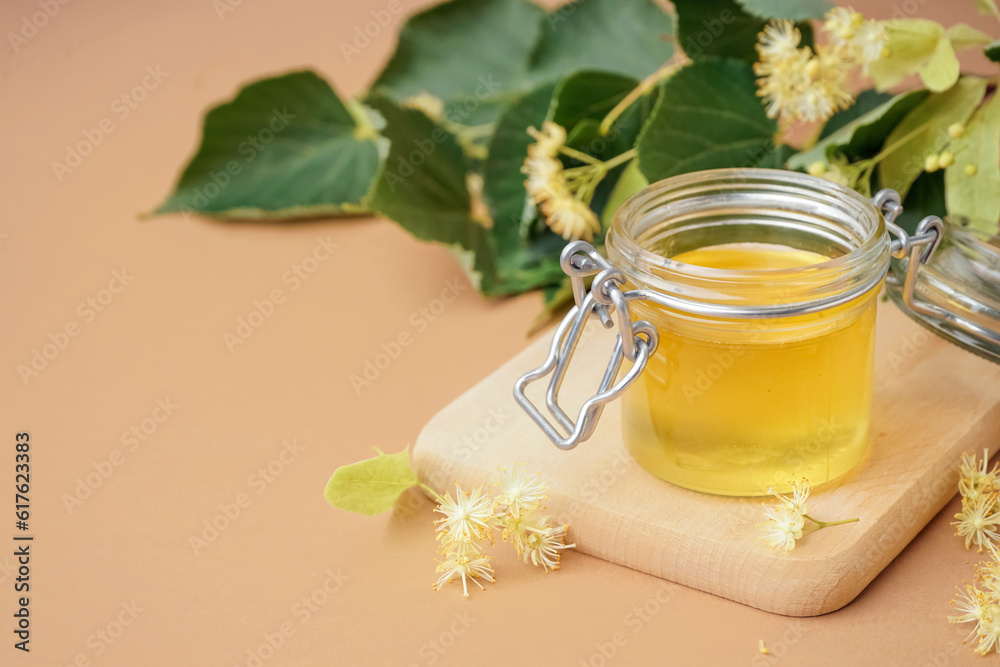 Wooden board with jar of linden honey on brown background