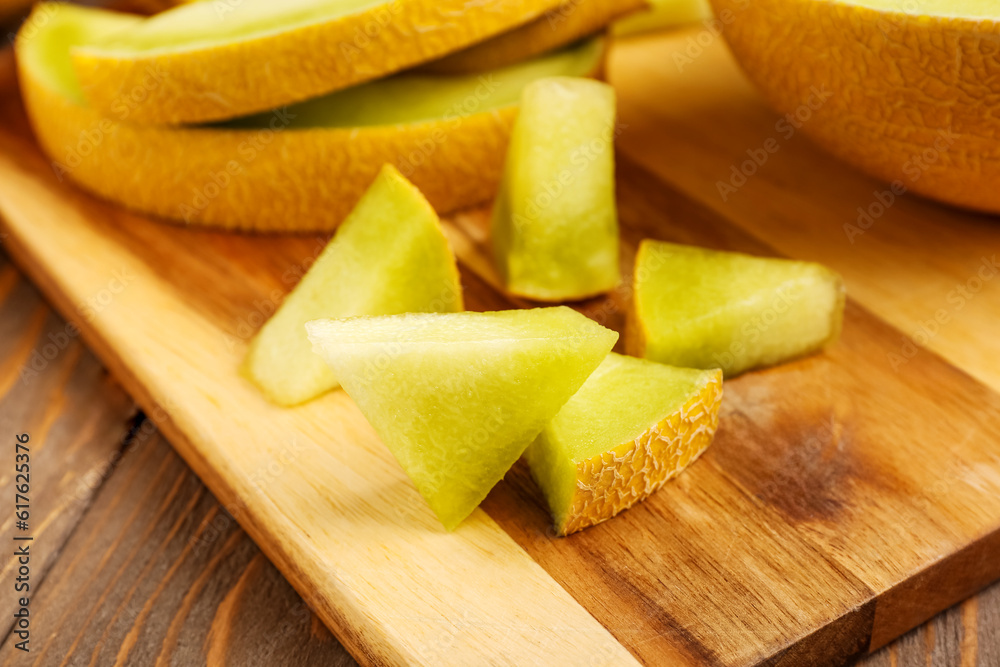 Board with pieces of sweet melon on wooden background, closeup