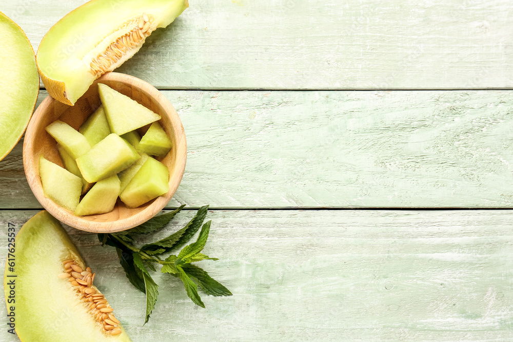 Bowl with pieces of sweet melon on green wooden background