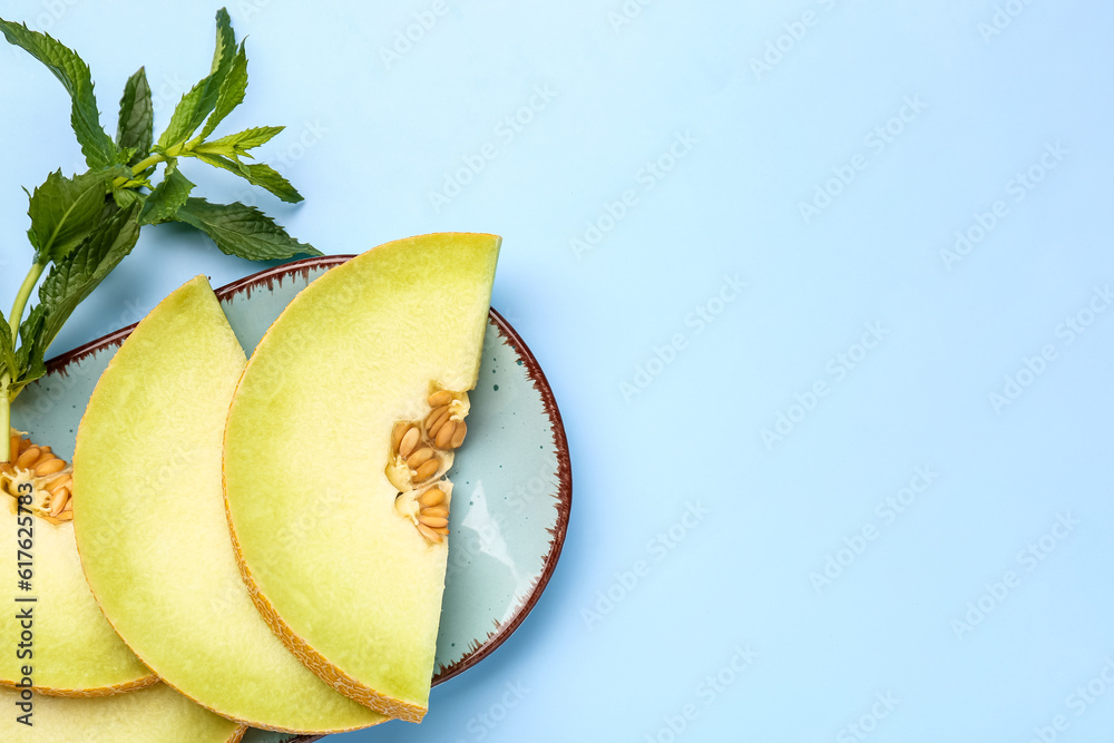 Plate with pieces of sweet melon and mint on blue background