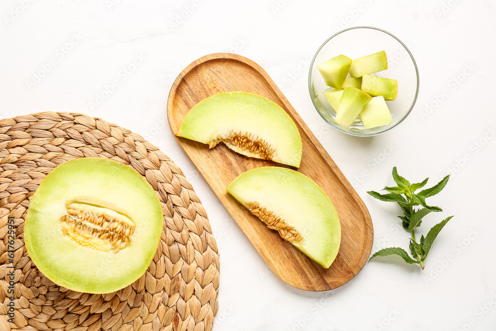 Wooden board and glass bowl with pieces of sweet melon on white background