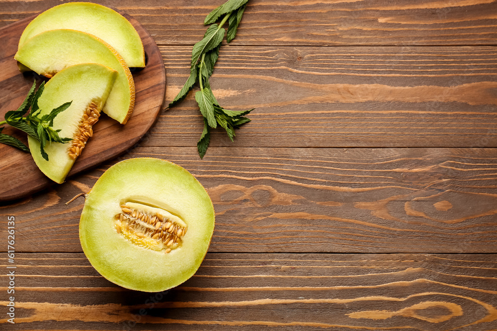 Half of sweet melon and board with pieces on wooden background