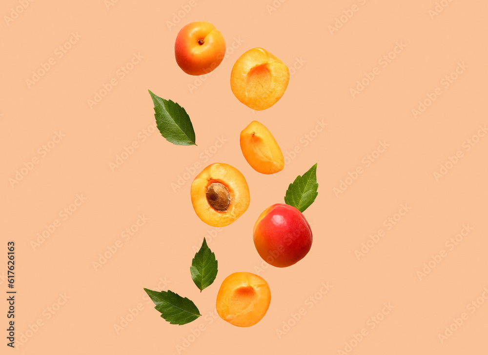 Flying fresh apricots with pieces and leaves on orange background