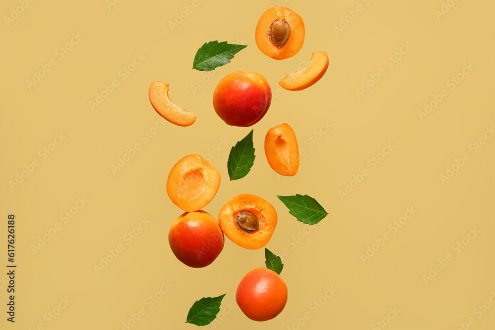 Flying fresh apricots with pieces and leaves on green background