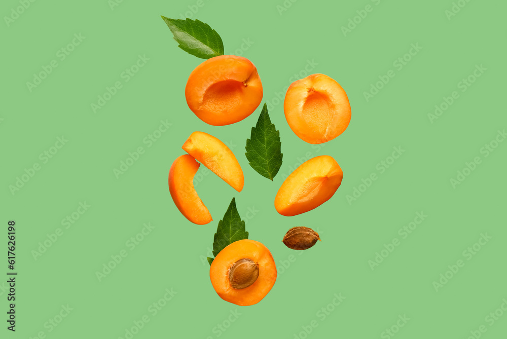 Flying halves of fresh apricot with pieces and leaves on green background