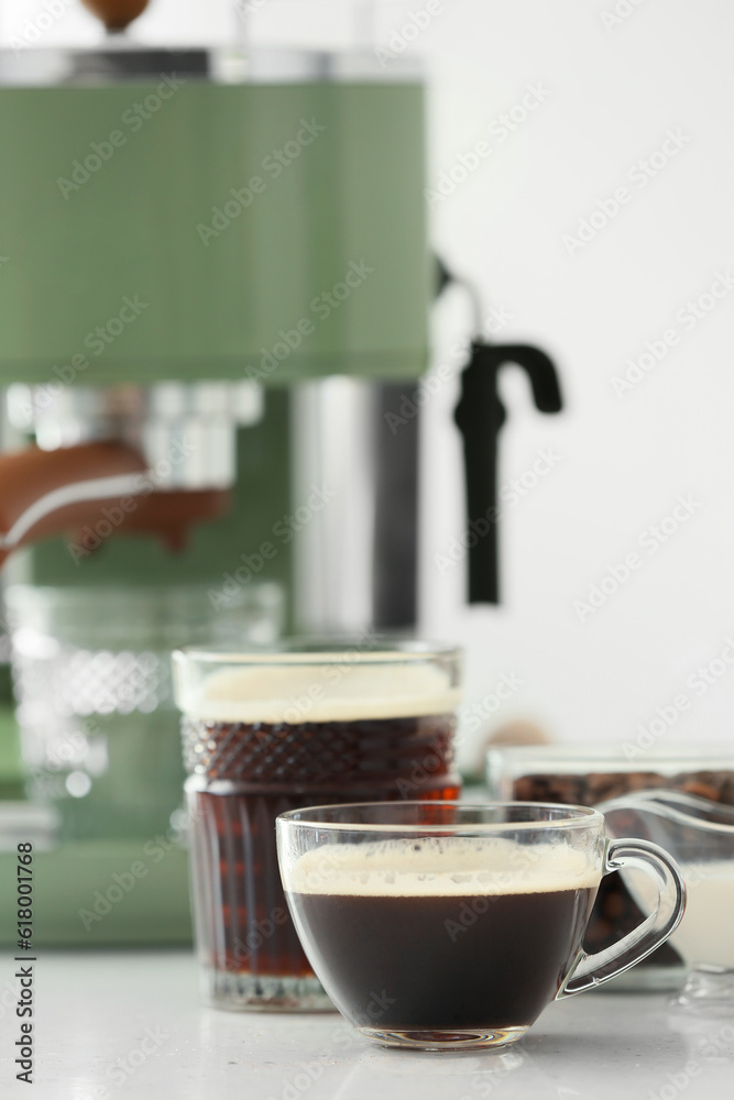 Cups of hot espresso and modern coffee machine on table in kitchen