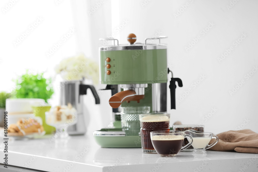 Modern coffee machine and cups of hot espresso on table in kitchen