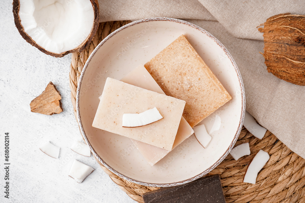 Composition with plate of natural soap bars and coconut on light background, closeup