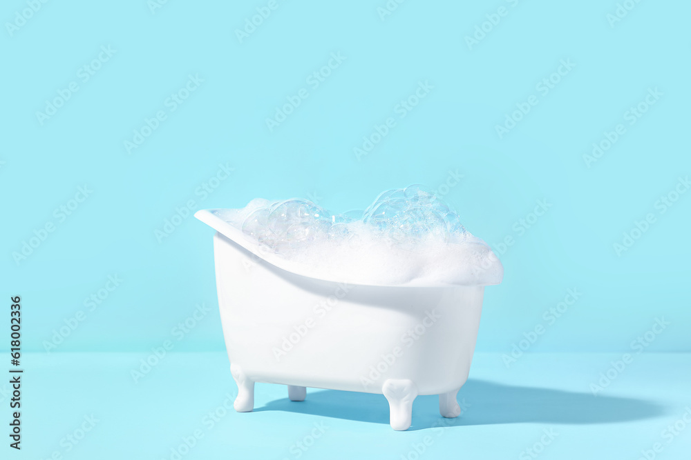 Small bathtub with foam on color background