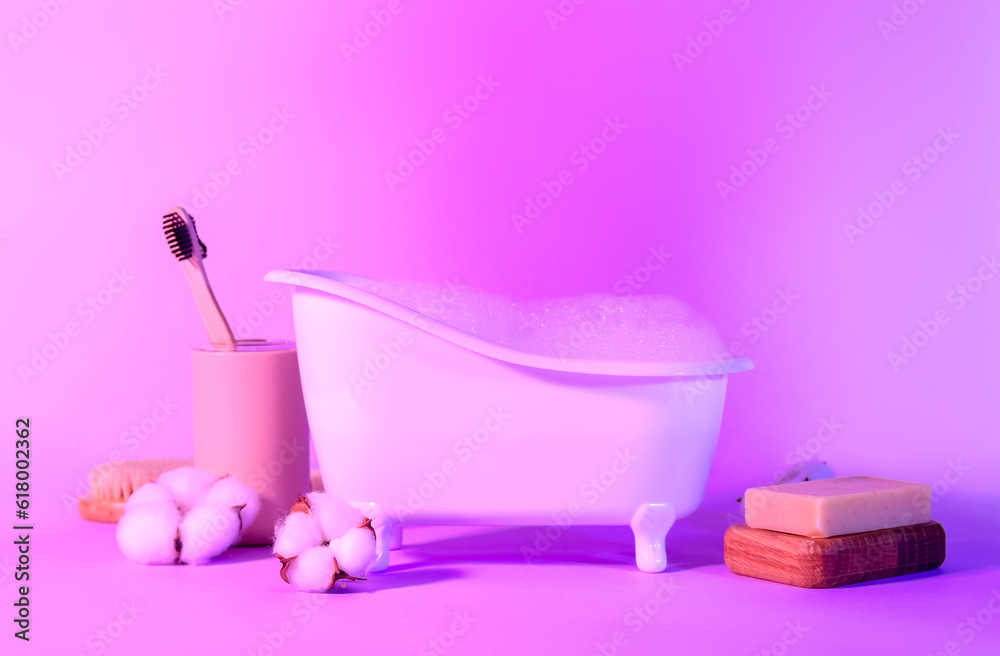 Small bathtub with foam, toothbrushes, soap and cotton flowers on color background