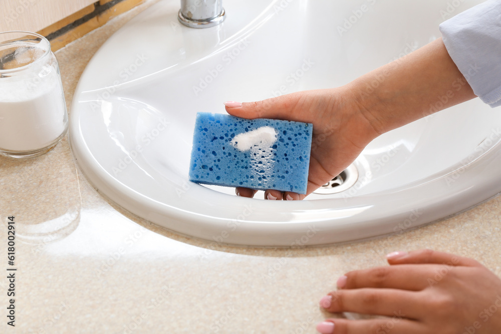 Woman cleaning white sink with baking soda and sponge, closeup