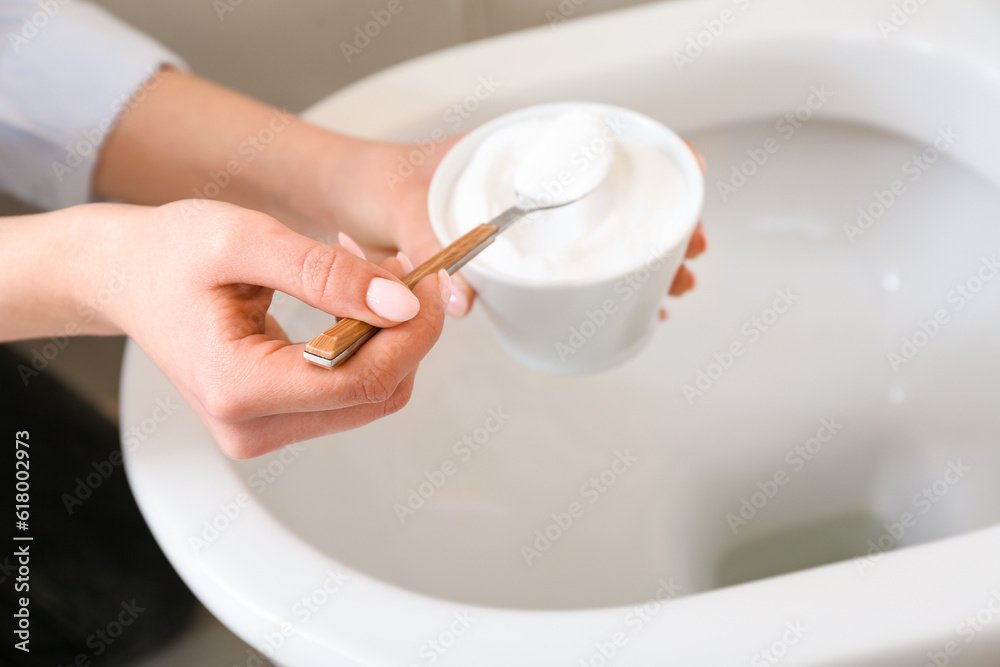 Woman cleaning white toilet bowl with baking soda, closeup