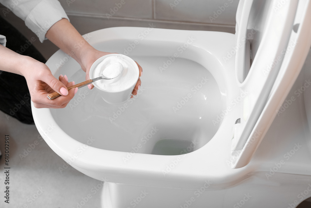 Woman cleaning white toilet bowl with baking soda