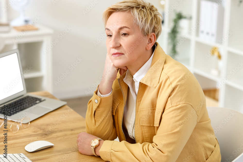 Thoughtful mature woman sitting at table in office