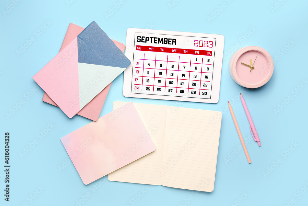 Modern tablet computer with calendar, notebooks, alarm clock and pencils on blue background