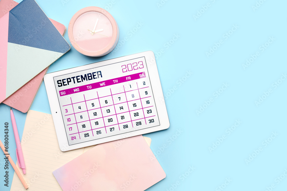 Modern tablet computer with calendar, notebooks, alarm clock and pencils on blue background