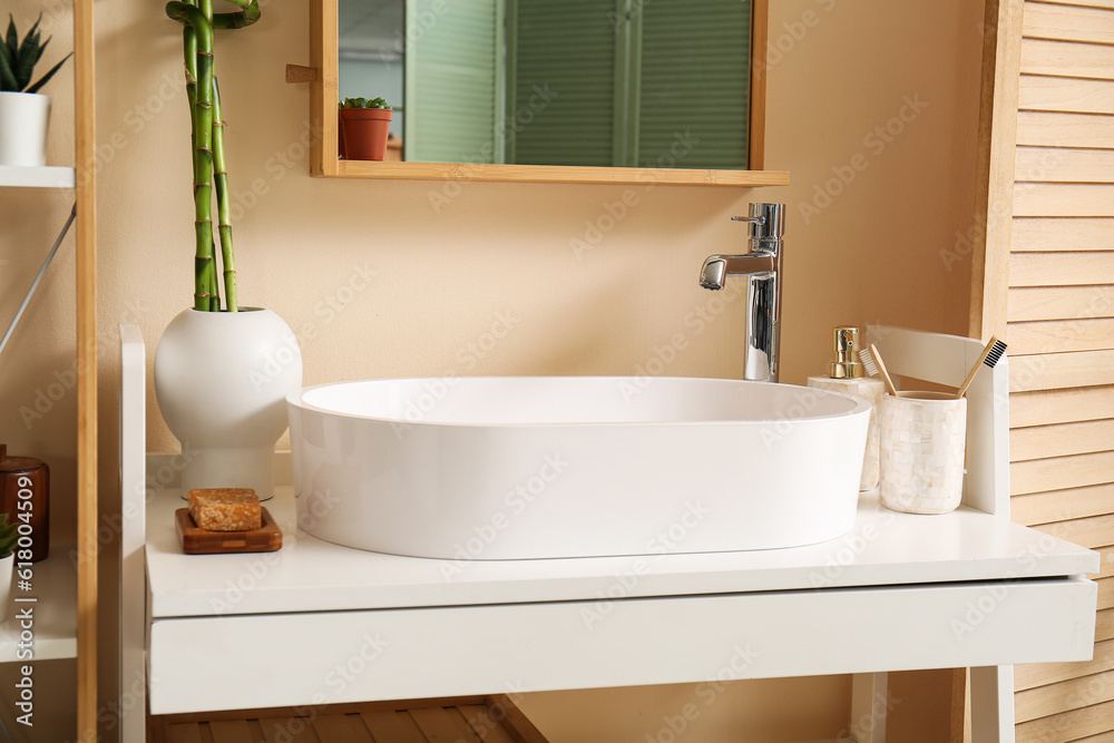 White sink, bath accessories and vase with bamboo stems on table in room