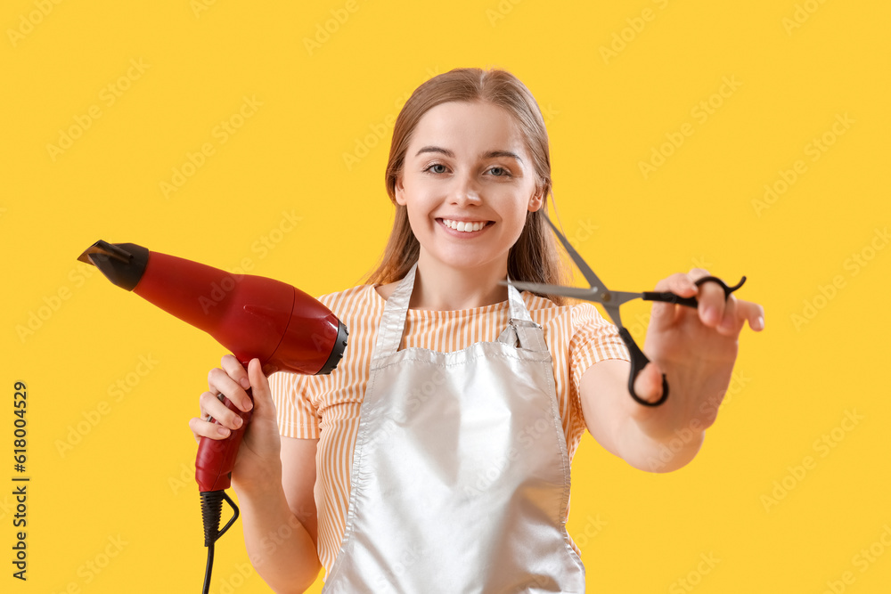 Female hairdresser with dryer and scissors on yellow background