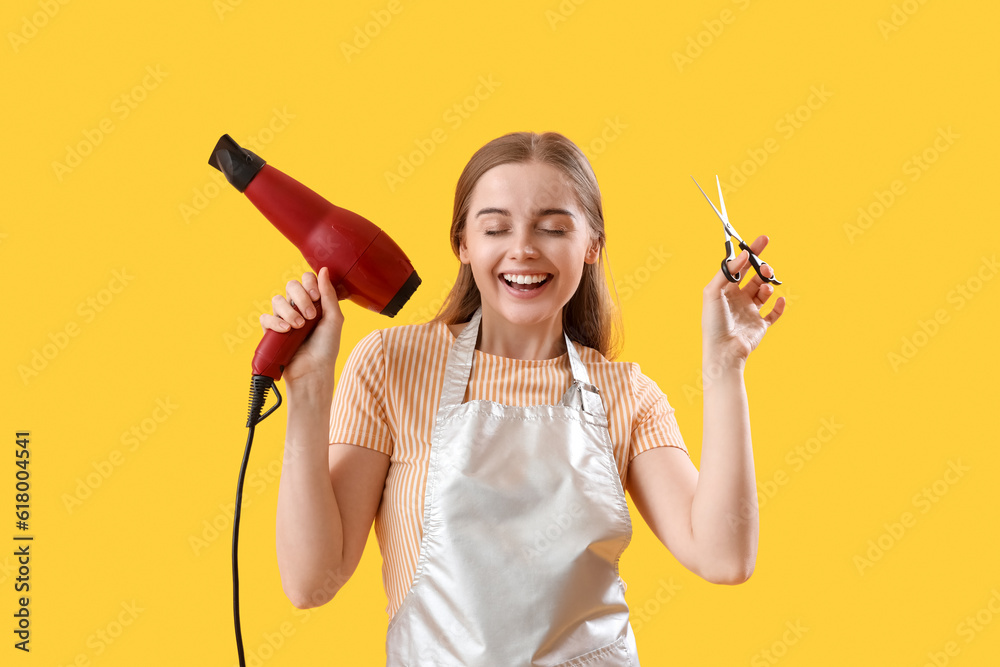 Female hairdresser with dryer and scissors on yellow background