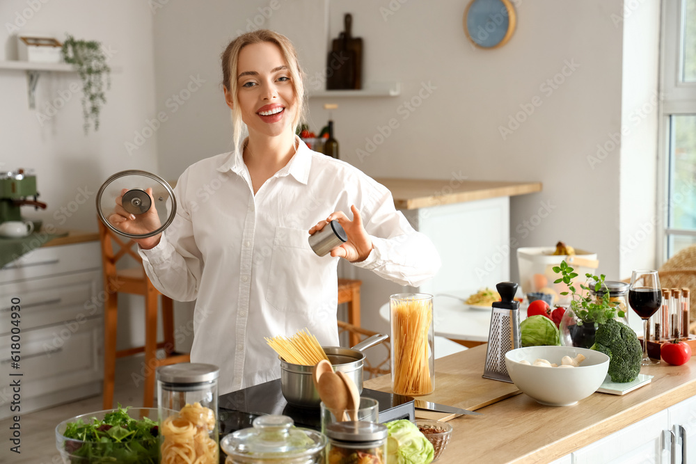 Young woman salting raw spaghetti in cooking pot at home