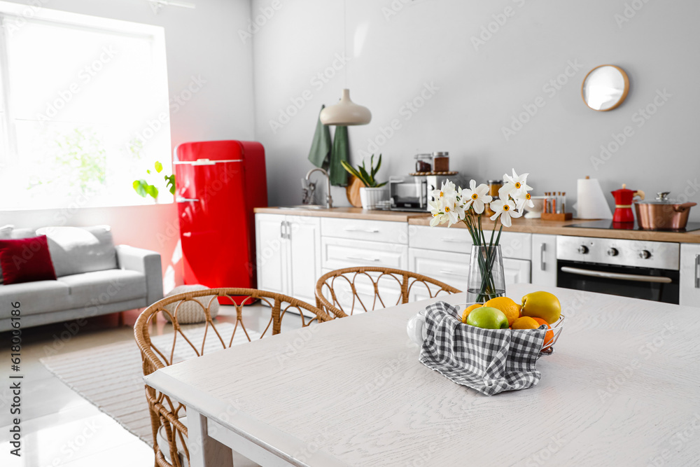 Basket with fruits and narcissus flowers on table in light kitchen