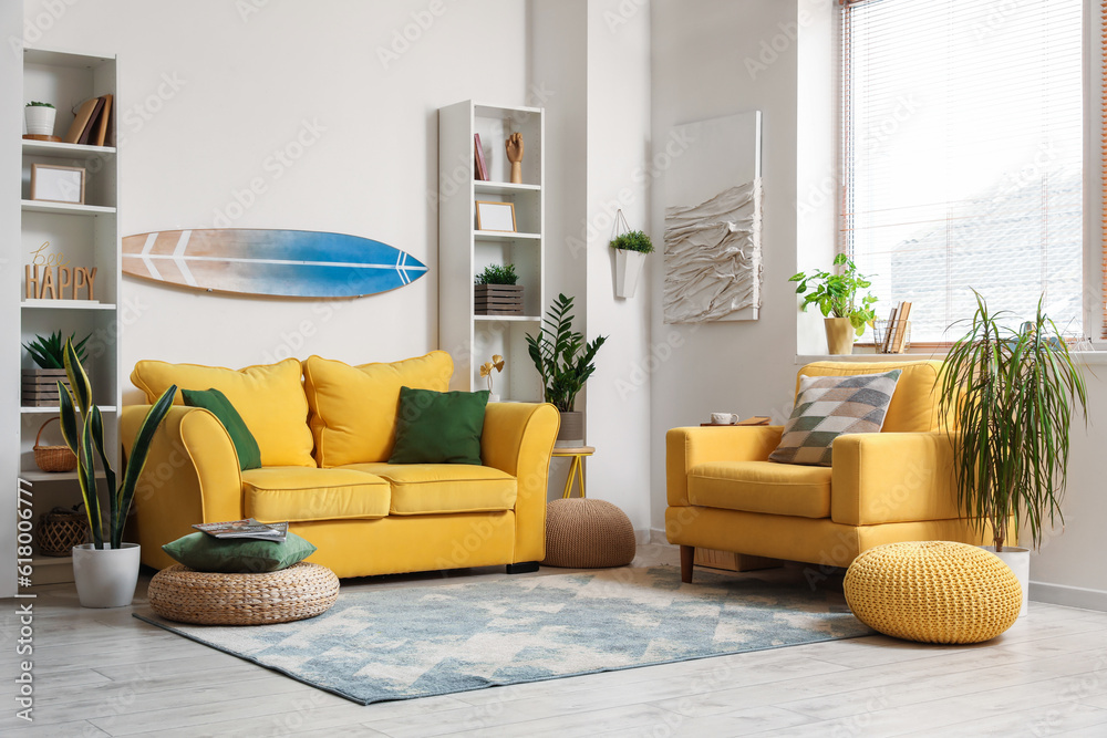 Interior of light living room with surfboard, yellow sofa and armchair