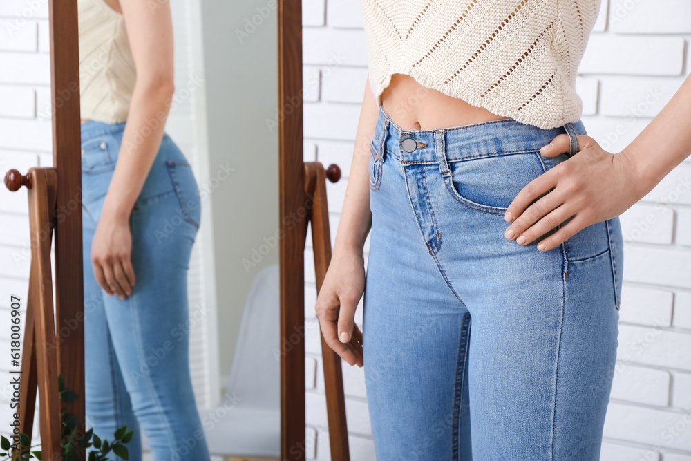 Young woman in stylish jeans near mirror in room