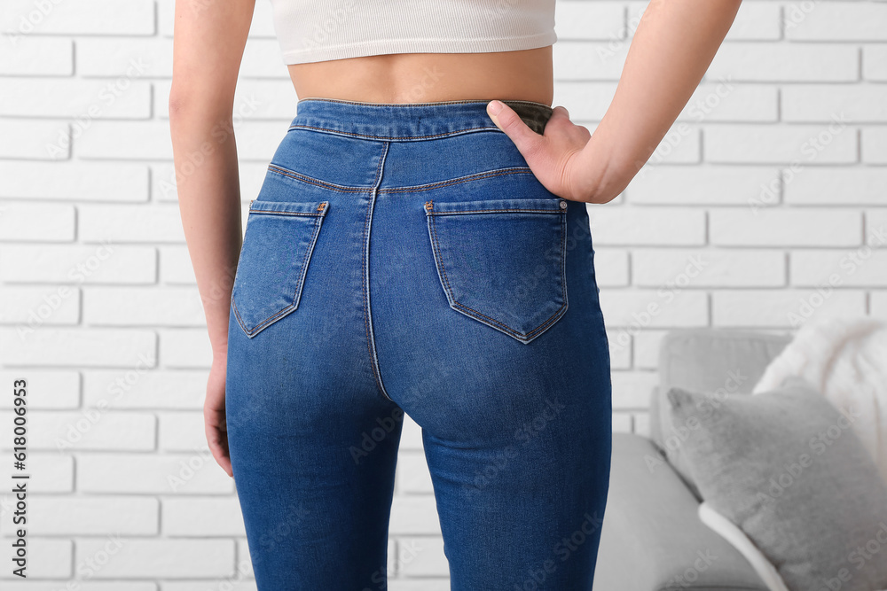 Young woman in stylish jeans near light brick wall